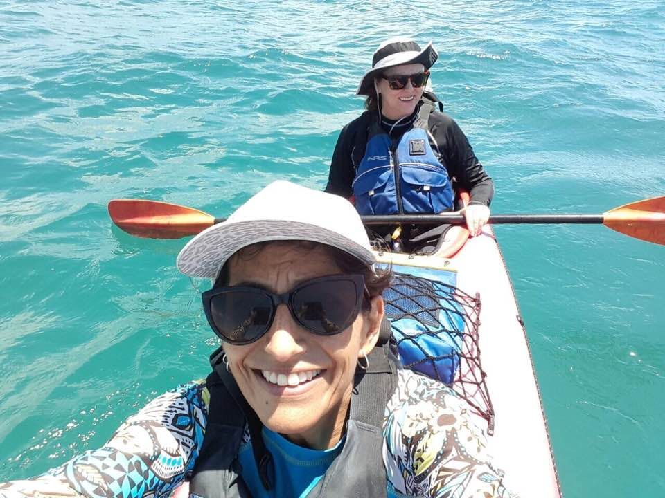 A woman wearing sunglasses and a hat is sitting in a kayak