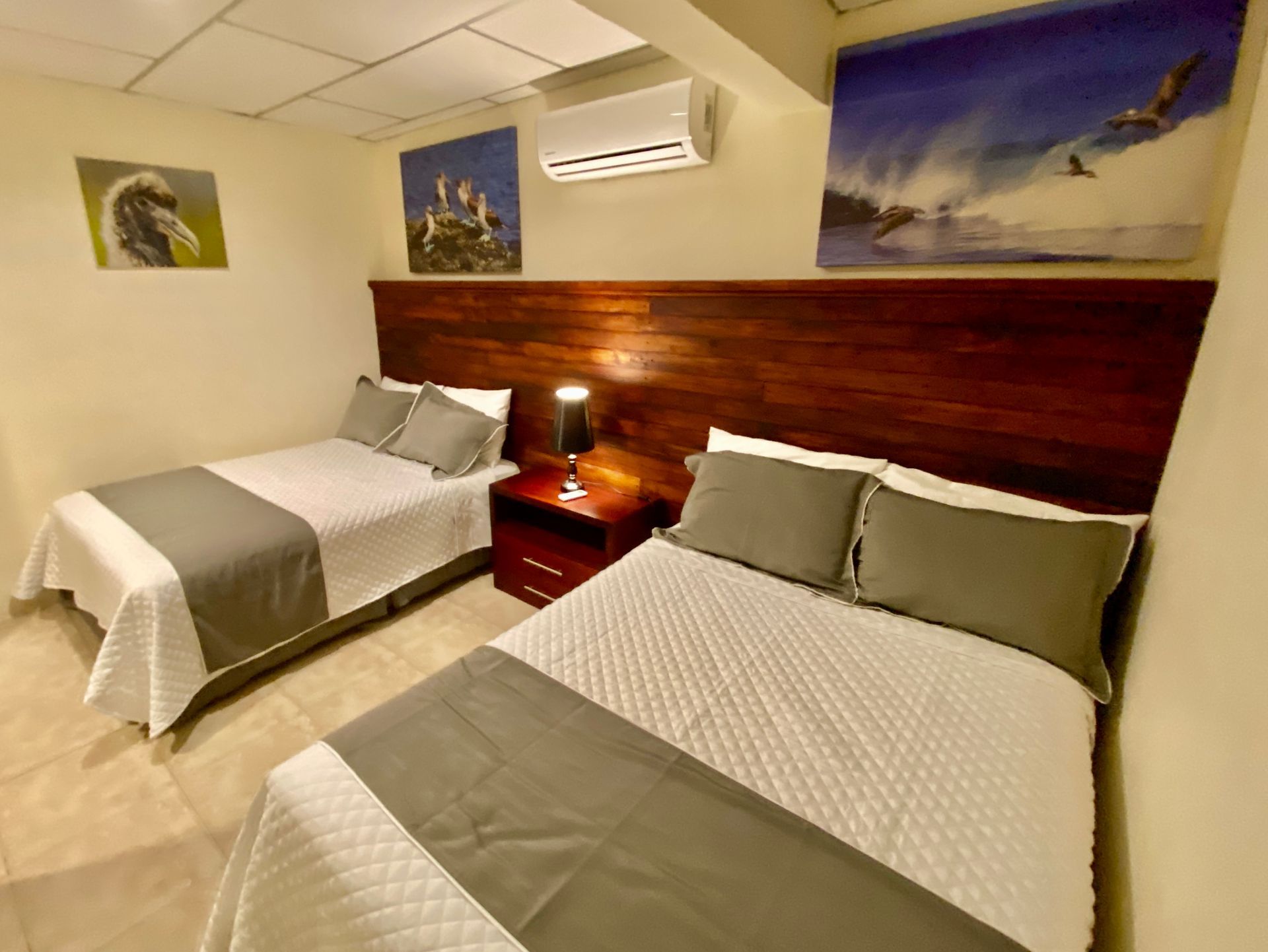 A hotel room with two beds, gray and white bedding, wooden headboards, and artwork on the walls.