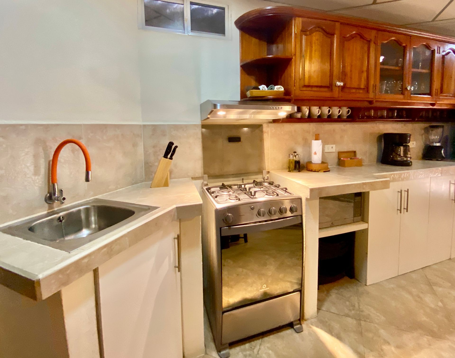 A small kitchen featuring a stainless steel stove, light-colored cabinets, and a sink with a rusty-colored faucet.