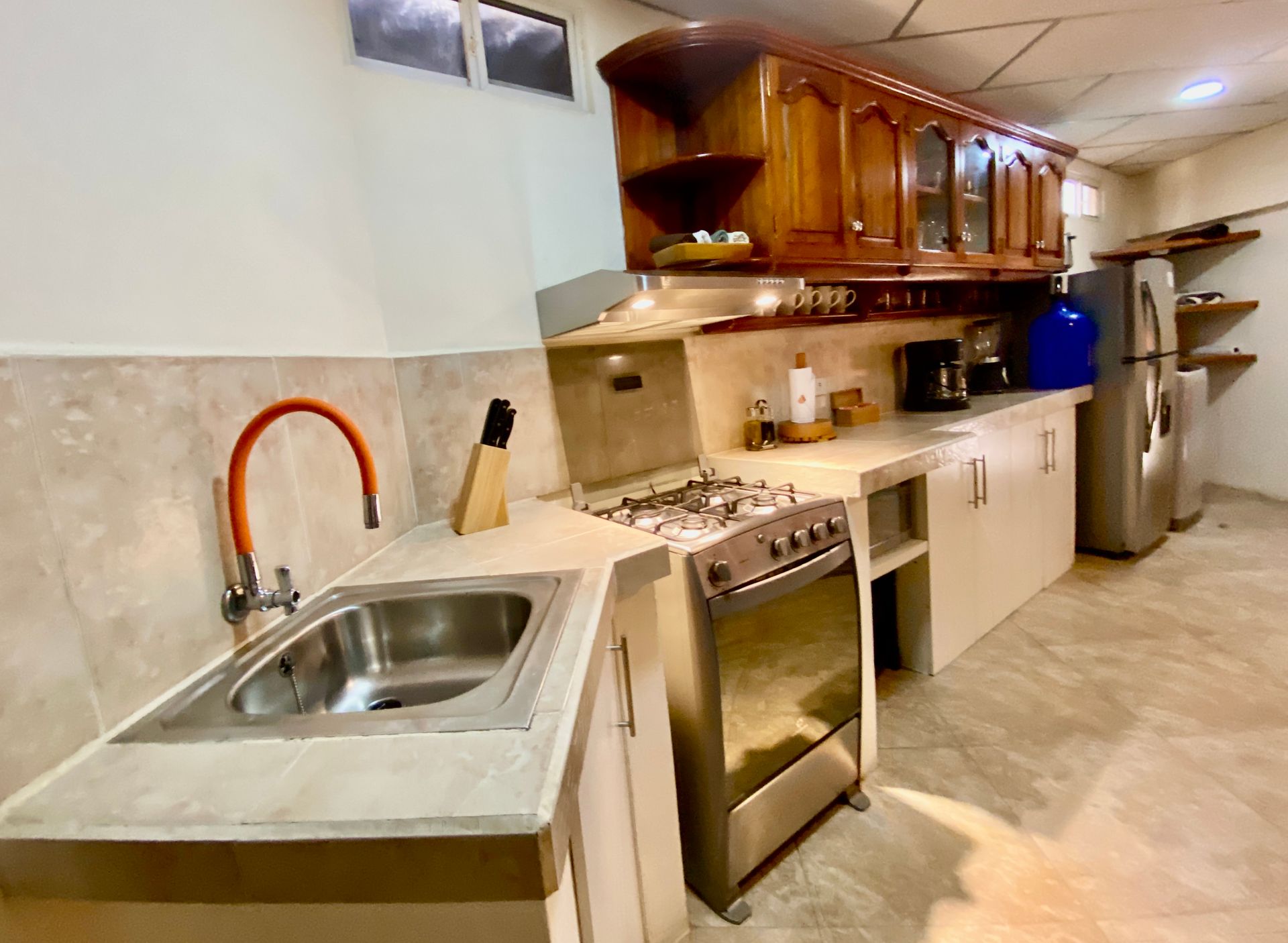 A kitchen with wooden cabinets, a stainless steel stove, sink, and refrigerator. The walls are light-colored.
