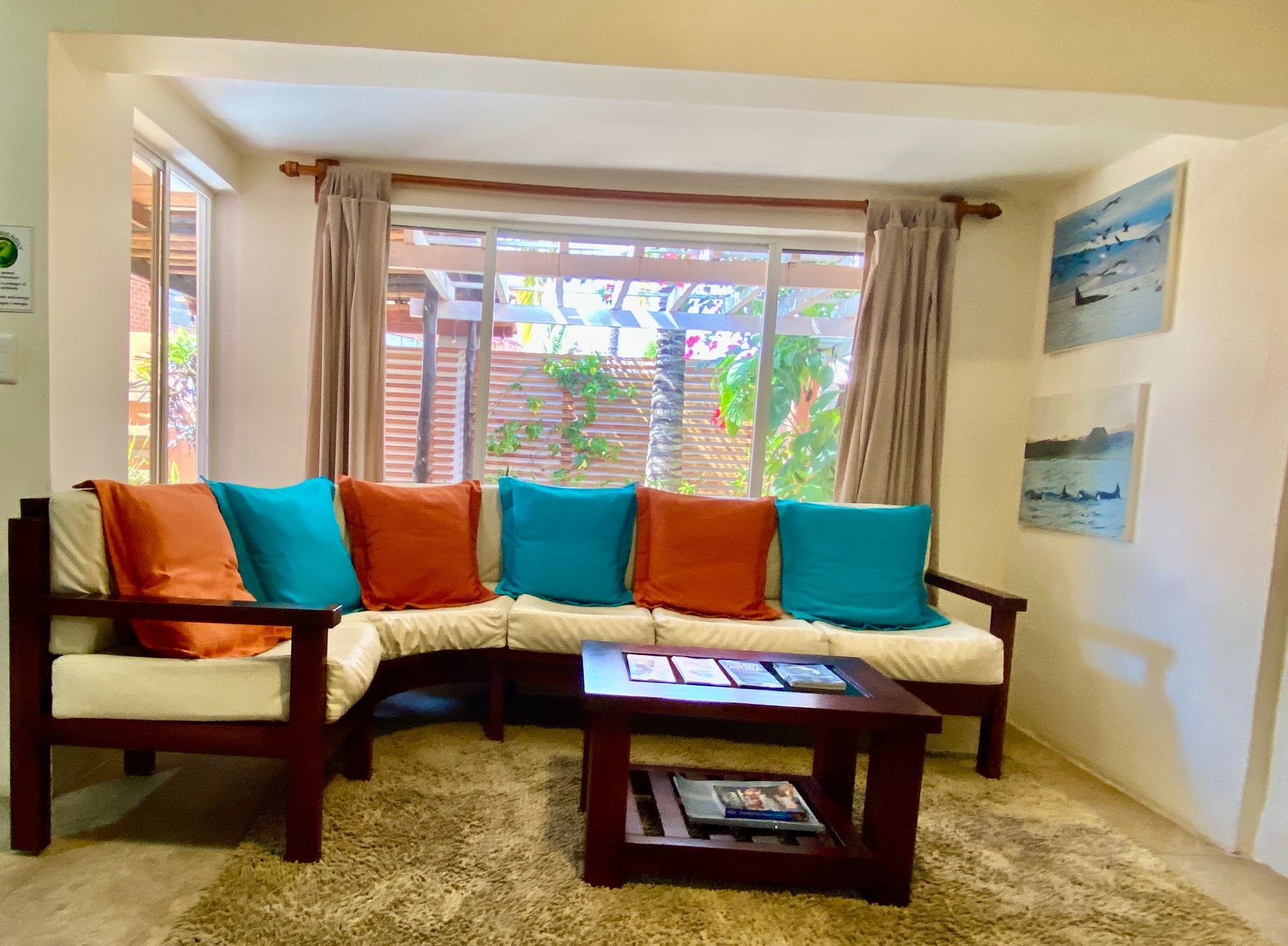 Living room with a wooden sofa adorned with blue and orange cushions, a coffee table, and artwork.