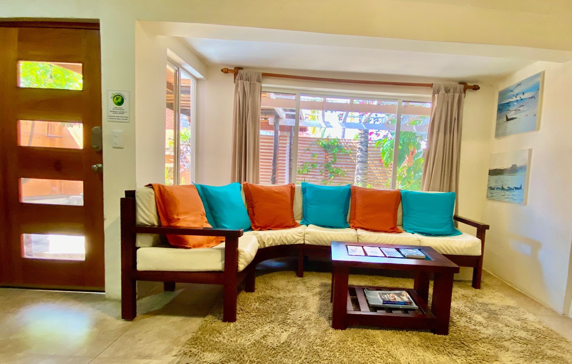 A cozy living room with a wooden sectional couch, orange and teal cushions, coffee table.