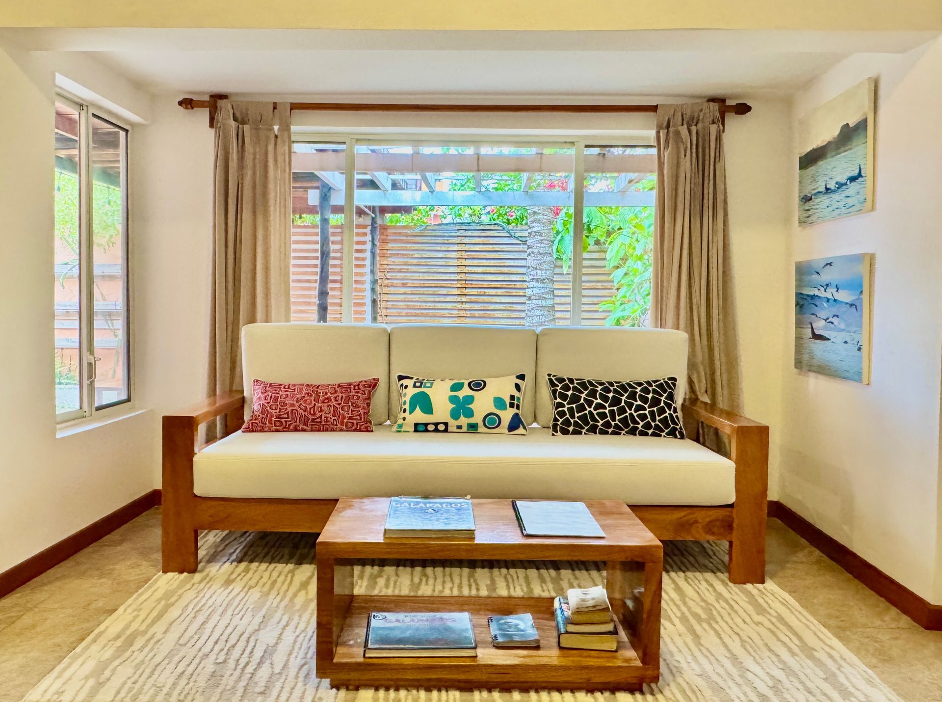 Living room with wooden furniture. Cream-colored couch with patterned pillows faces a coffee table.