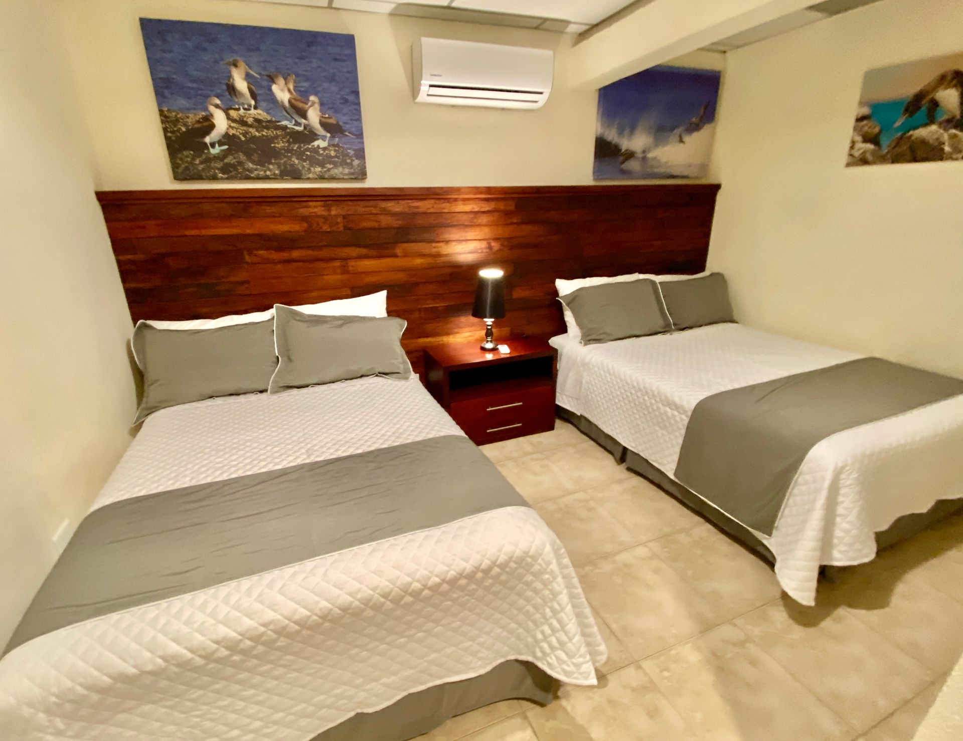 A hotel room with two beds, grey and white bedding, a wooden headboard, and nature artwork on the walls.