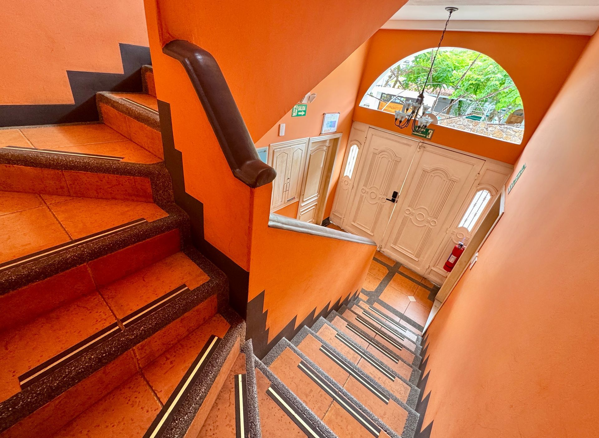 Orange staircase leading down to a doorway with arched top and double doors. Brown handrail, tiled steps.