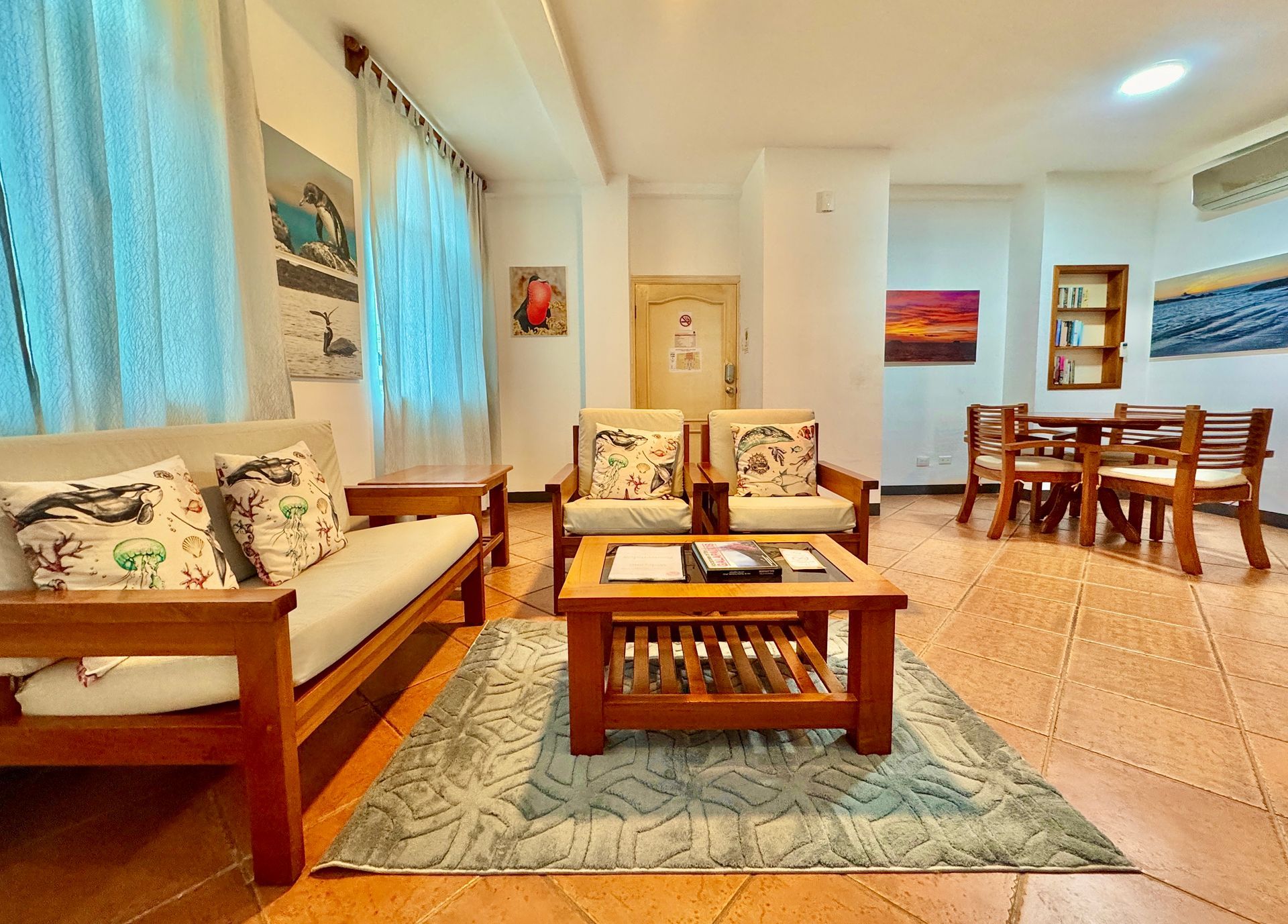 Bright living room with sofa, coffee table, dining set, blue curtains, and tiled floor