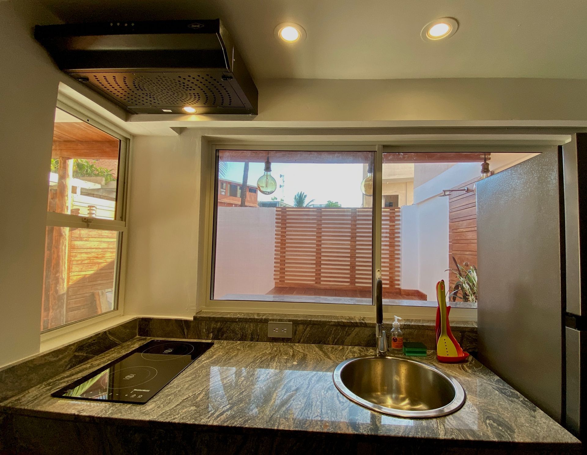 Kitchen with granite countertop, sink, and cooktop, looking out to a small yard through a sliding window.