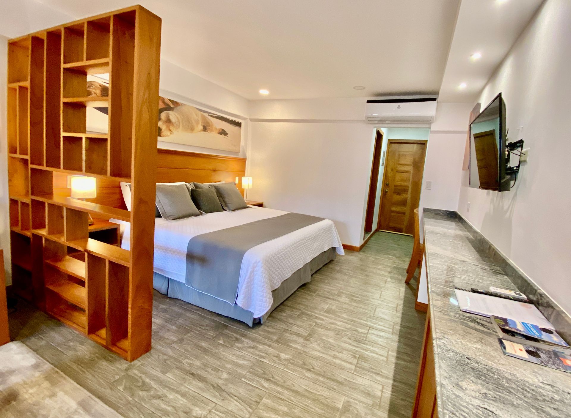 Cozy hotel room with a wooden bookshelf, a bed, and a desk with a TV mounted on the wall.
