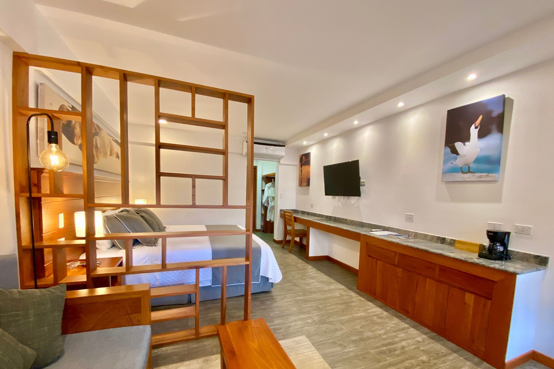 A modern studio apartment featuring a wooden room divider, a bed, a desk, and a television.