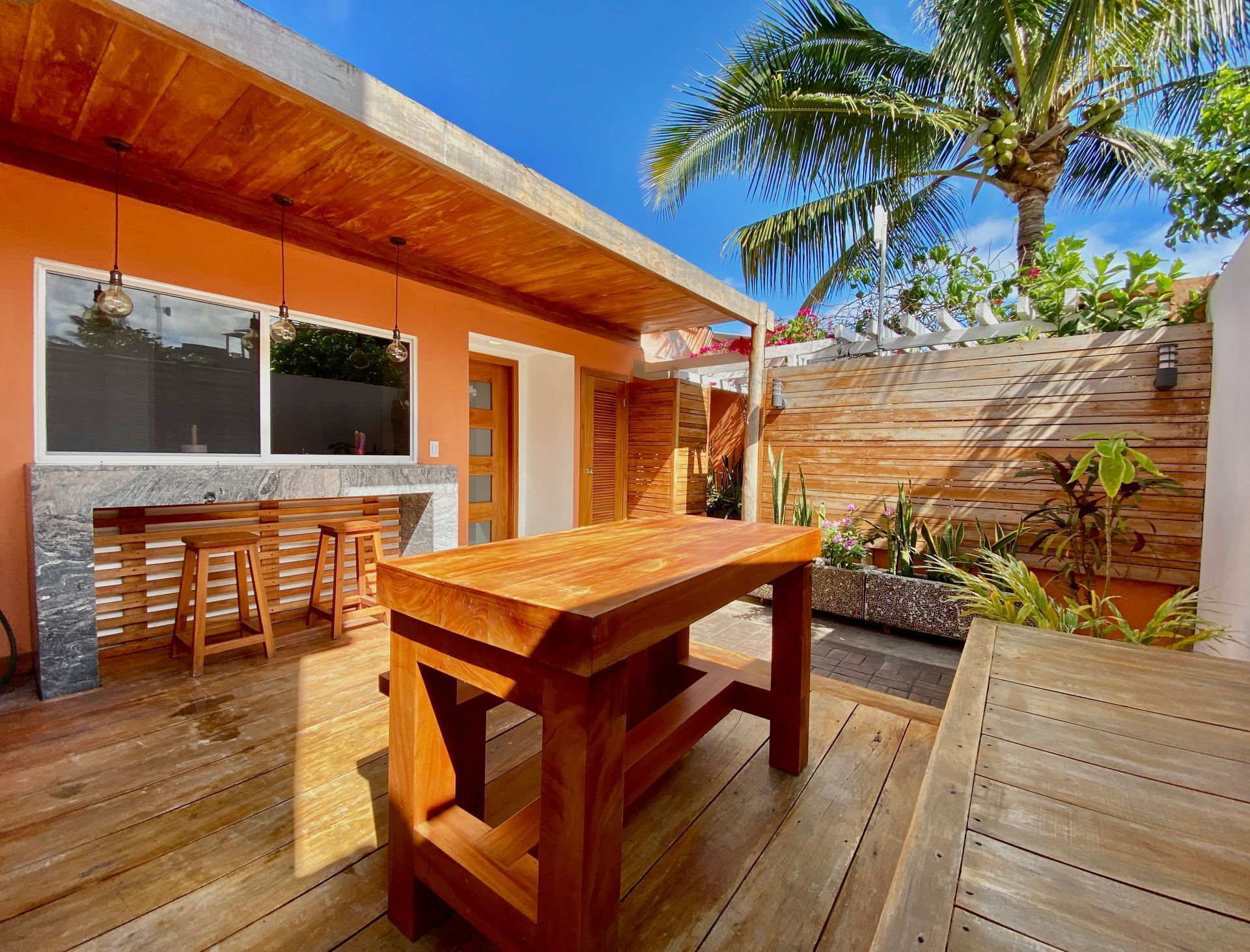 Outdoor patio with wooden furniture, orange walls, and a blue sky.
