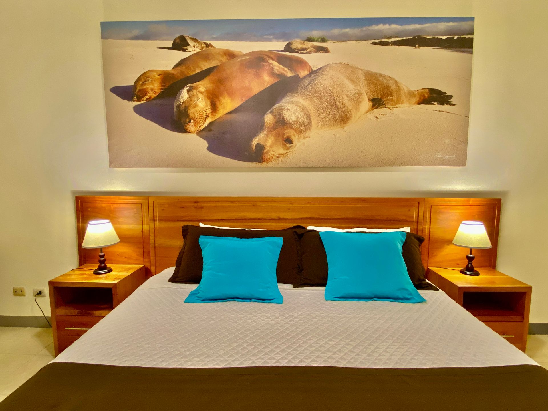 Bedroom with a bed made with gray bedding, teal pillows, and a brown bed skirt.