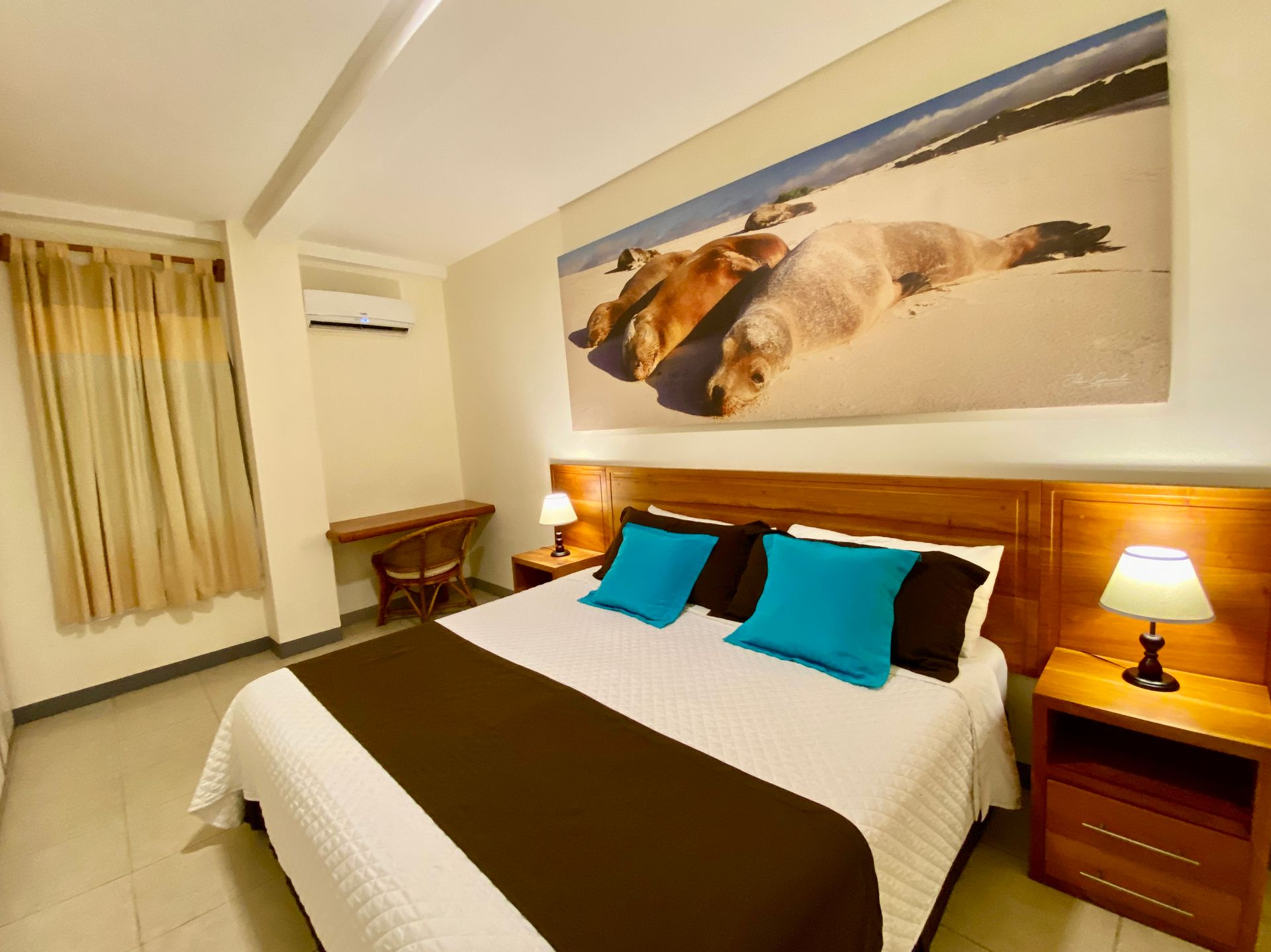 Bedroom with a large bed, blue pillows, and a brown bed runner. A seal photo is on the wall above the bed, with a desk.