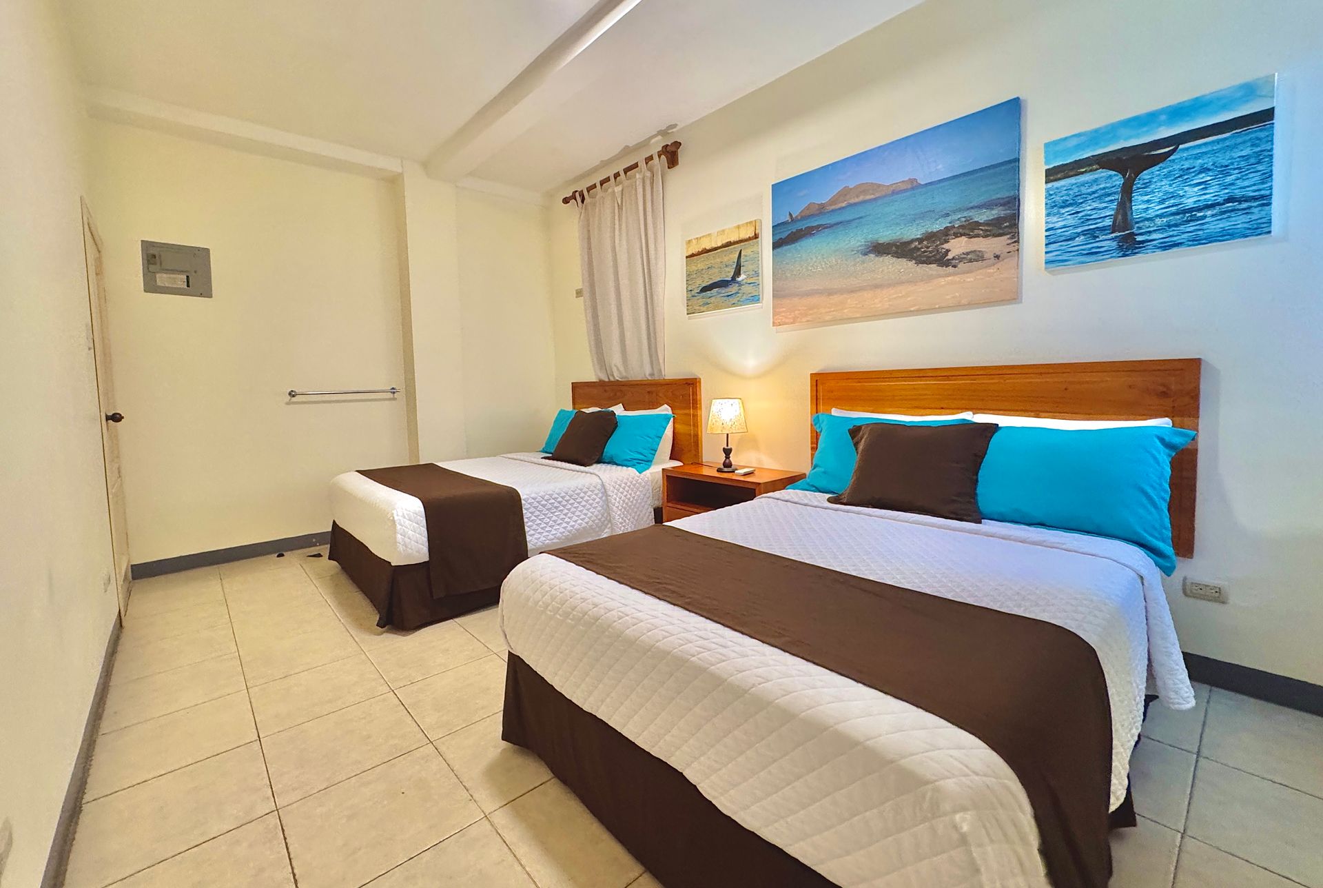 Two twin beds with brown and white bedding in a well-lit room with beach landscape art on the wall.