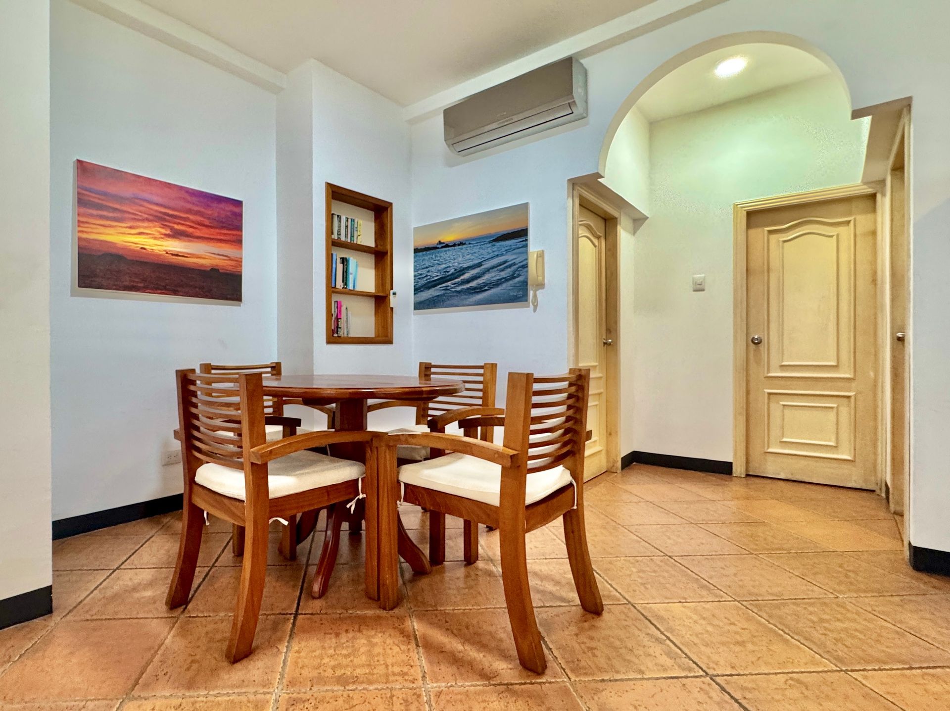 A dining area with a wooden table and chairs, artwork on the walls, and doorways leading to other rooms.
