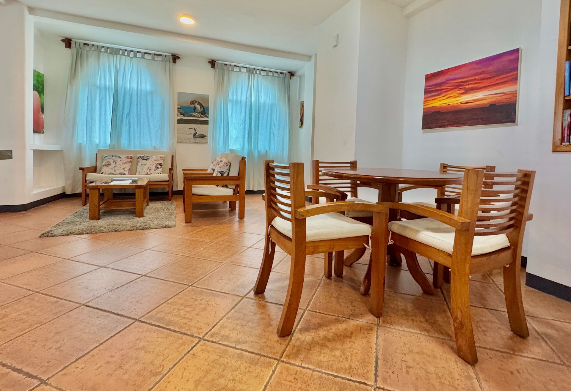 A brightly lit dining area with a wooden table and chairs, a seating area with a couch and chairs.