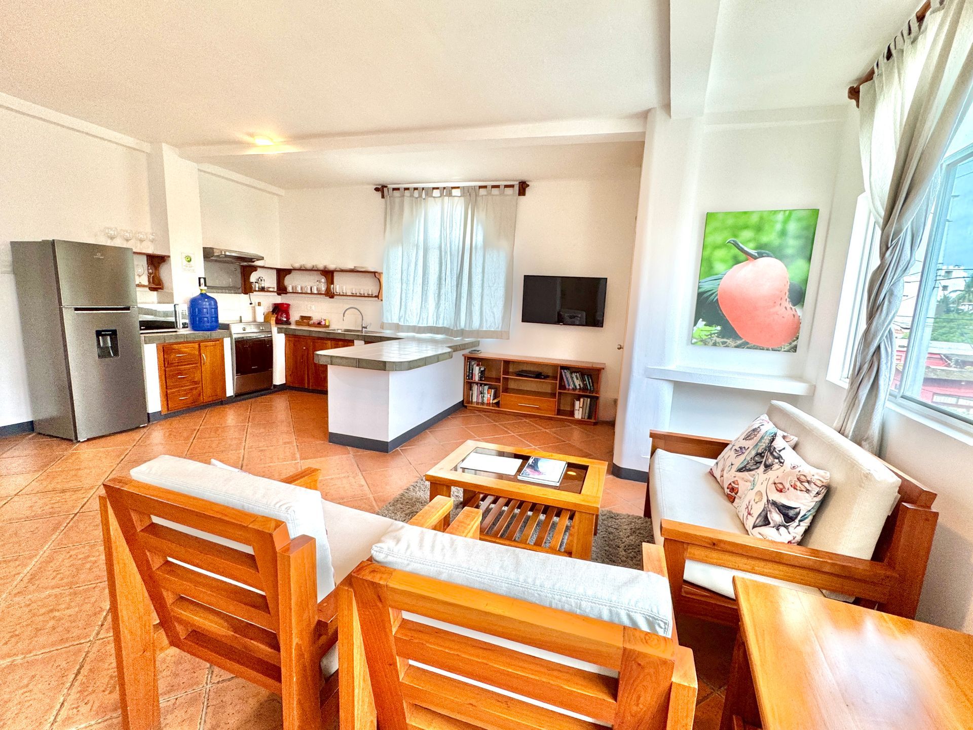 Living area and kitchen with wooden furniture and a stainless steel refrigerator.