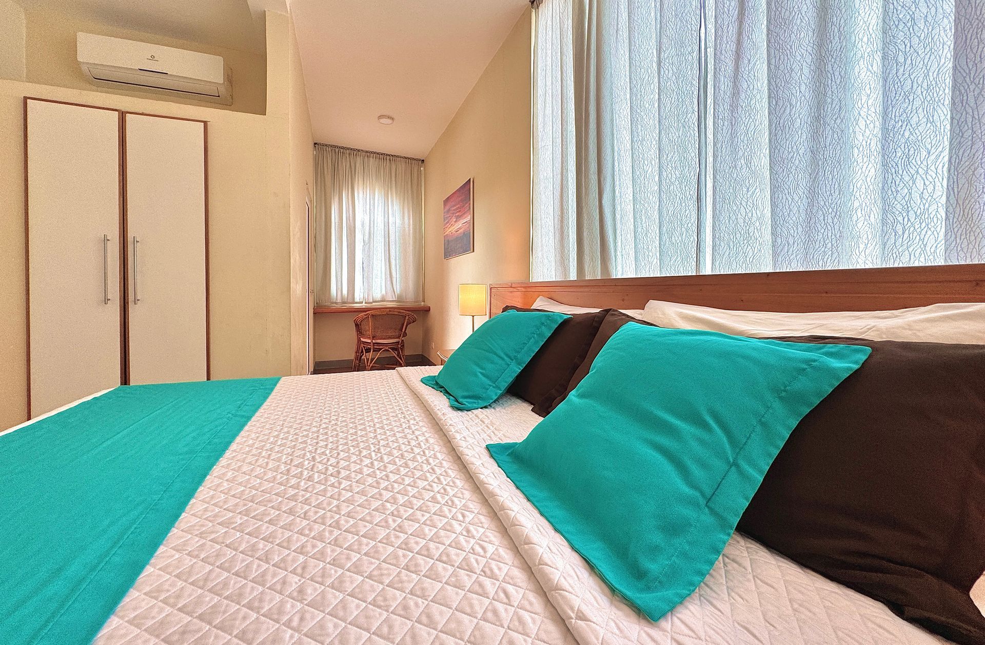 Bedroom with a bed covered in a teal and white quilt, teal pillows, and brown pillows.