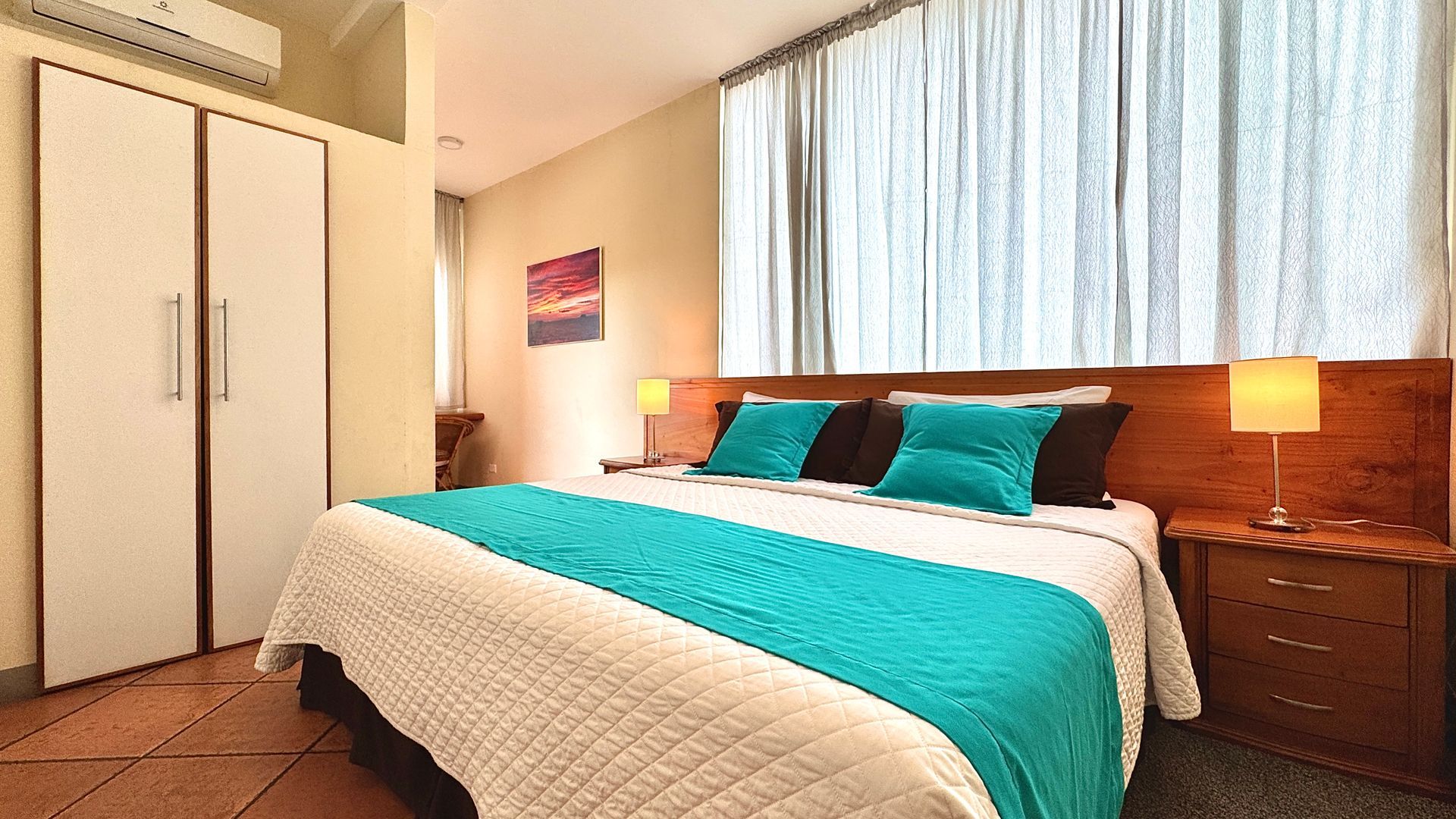 Bedroom with a king-sized bed featuring a turquoise throw, matching pillows, and wooden nightstands with lamps.