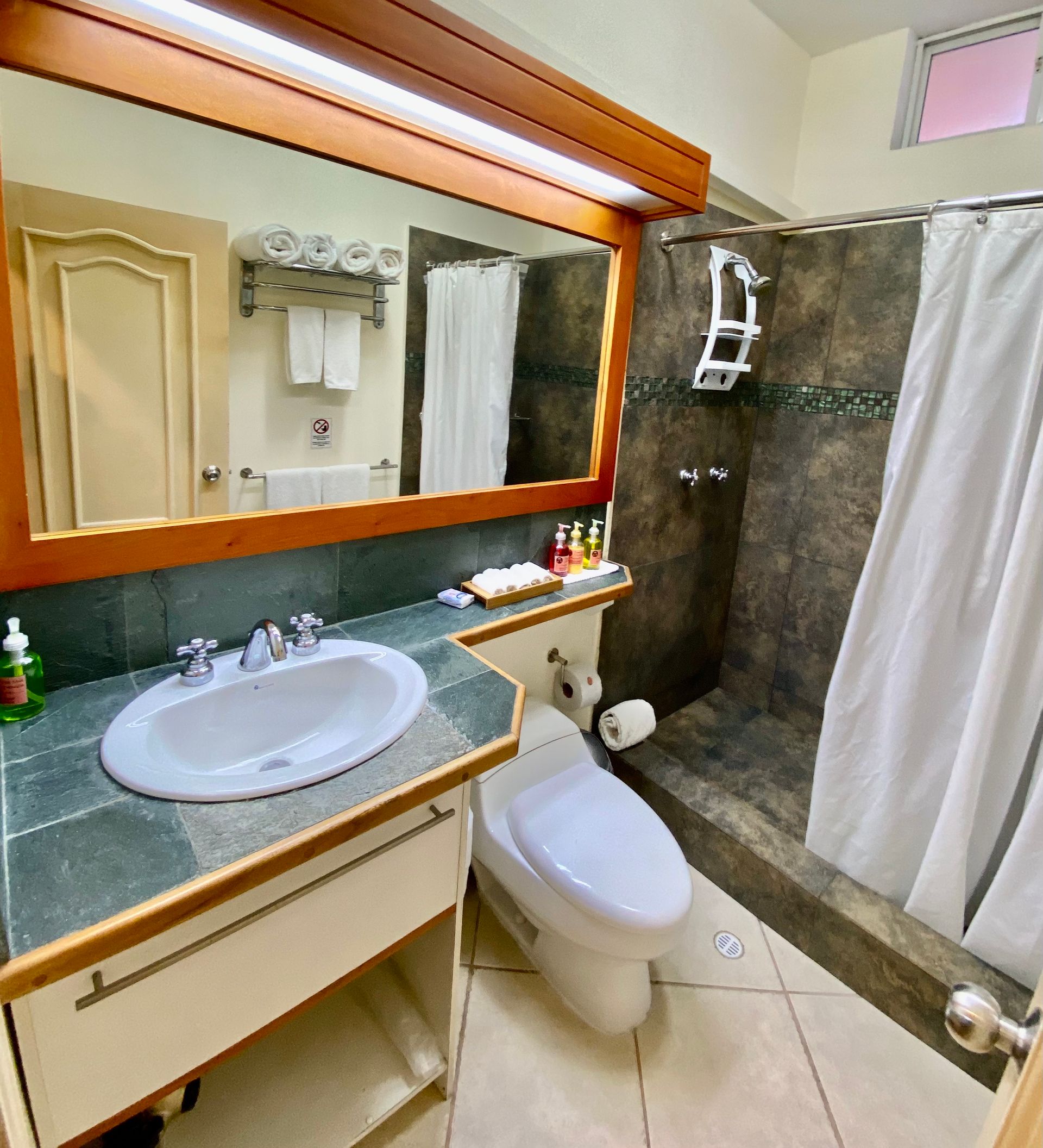 Bathroom with a sink, toilet, and shower. The shower has a white curtain, and the sink area.