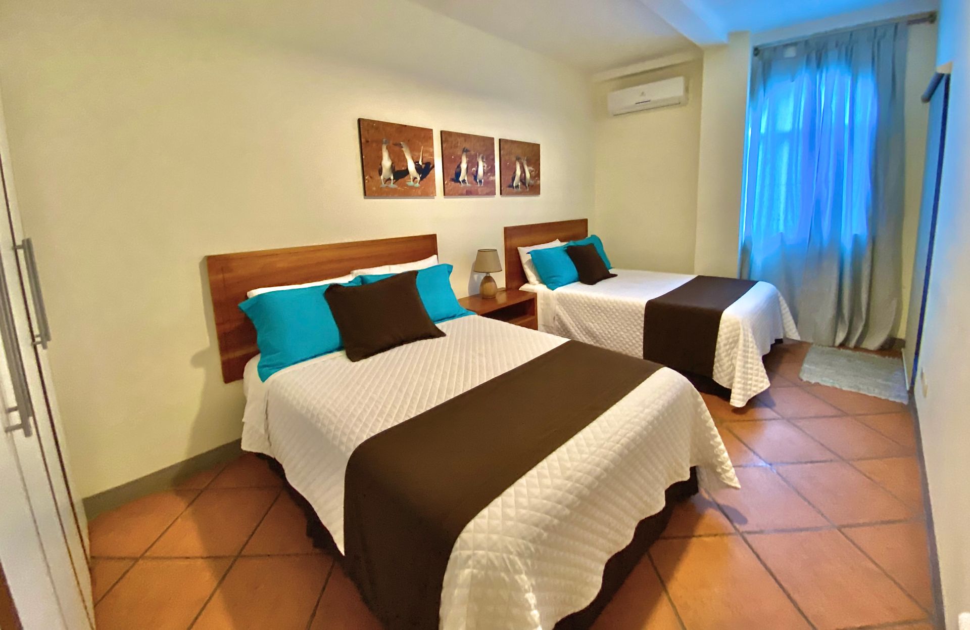 Two beds in a room with brown and white bedding, teal pillows, and wooden headboards. Artwork hangs above the beds.