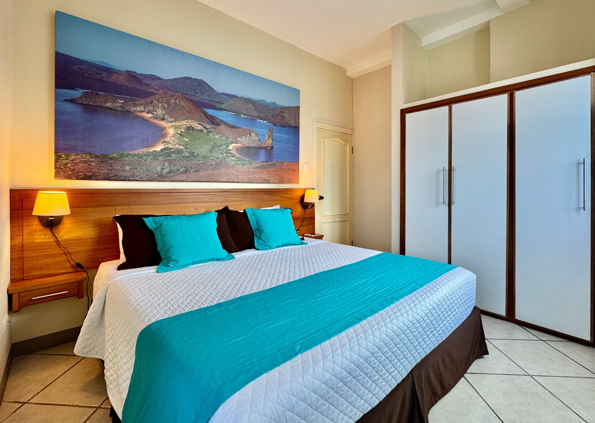 Bedroom with a king-sized bed, turquoise accents, landscape art above the headboard, and white closet.