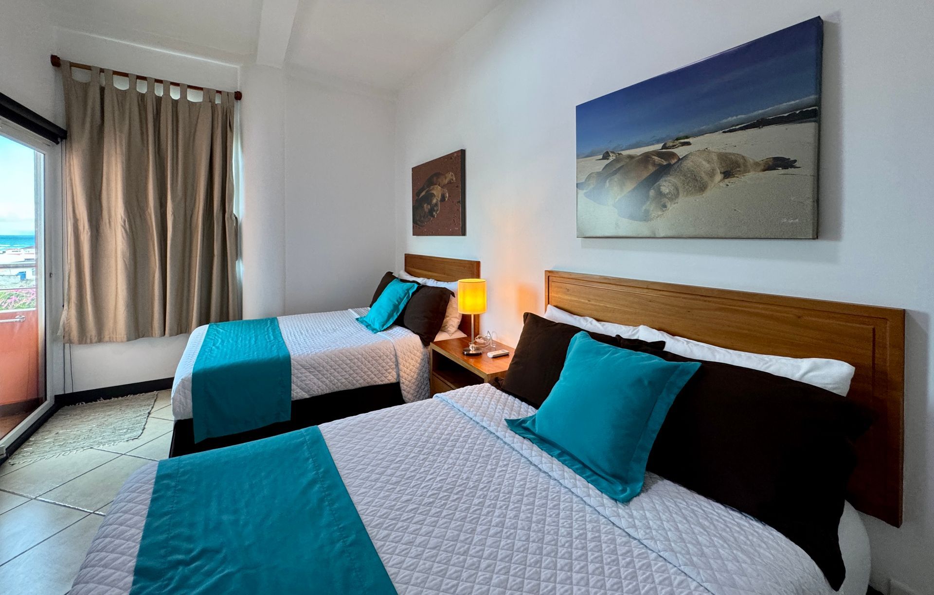 Two twin beds in a bright bedroom. Teal blankets and pillows contrast with the white bedspreads