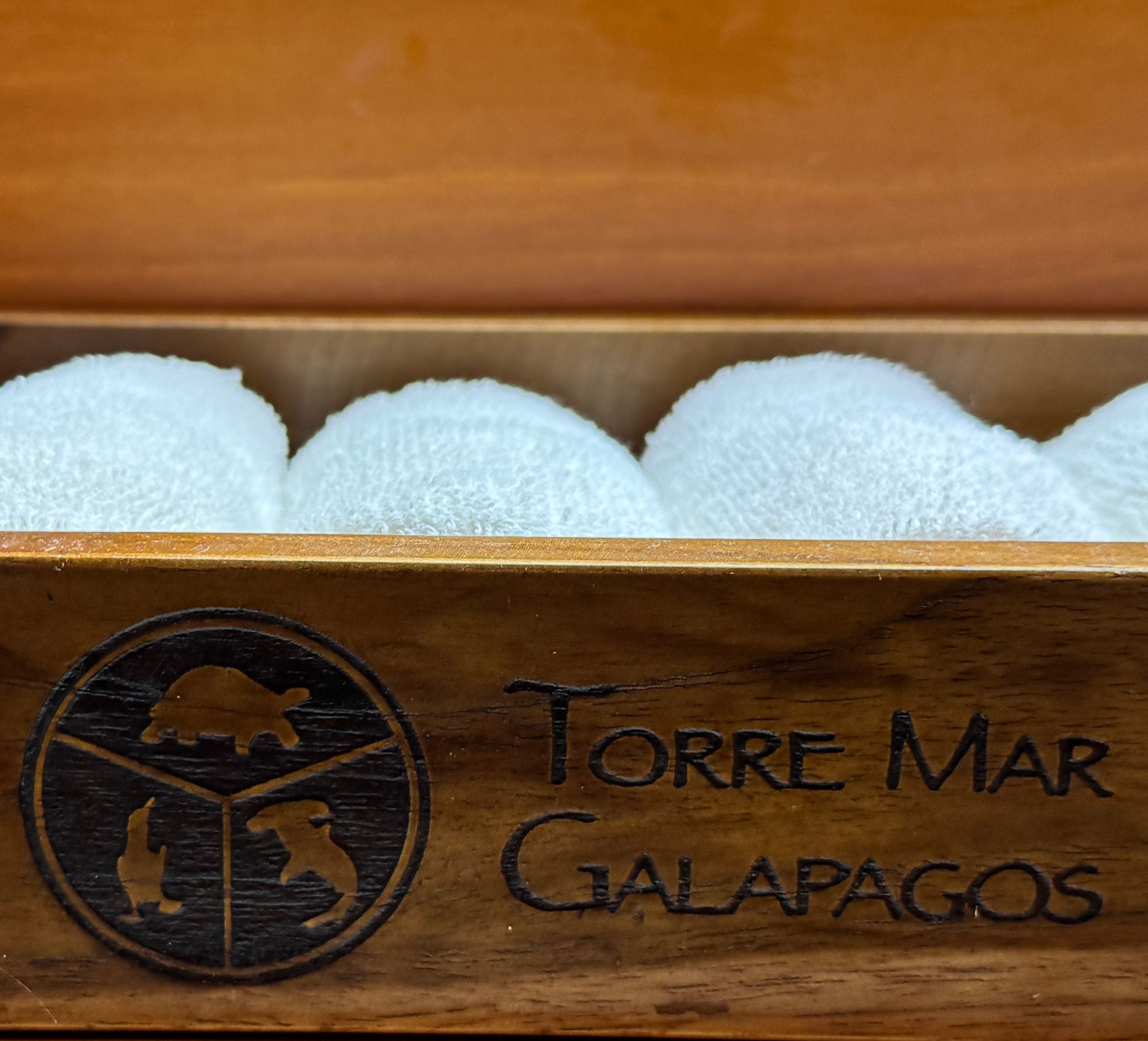 Wooden box with the Torre Mar Galapagos logo, containing rolled white washcloths.