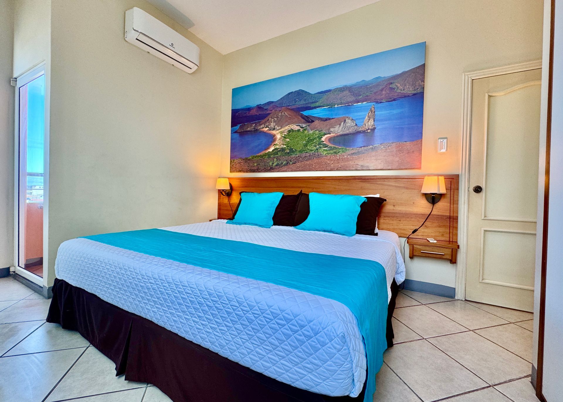 A bedroom with a large bed, turquoise bedding, and a landscape photo above the headboard.