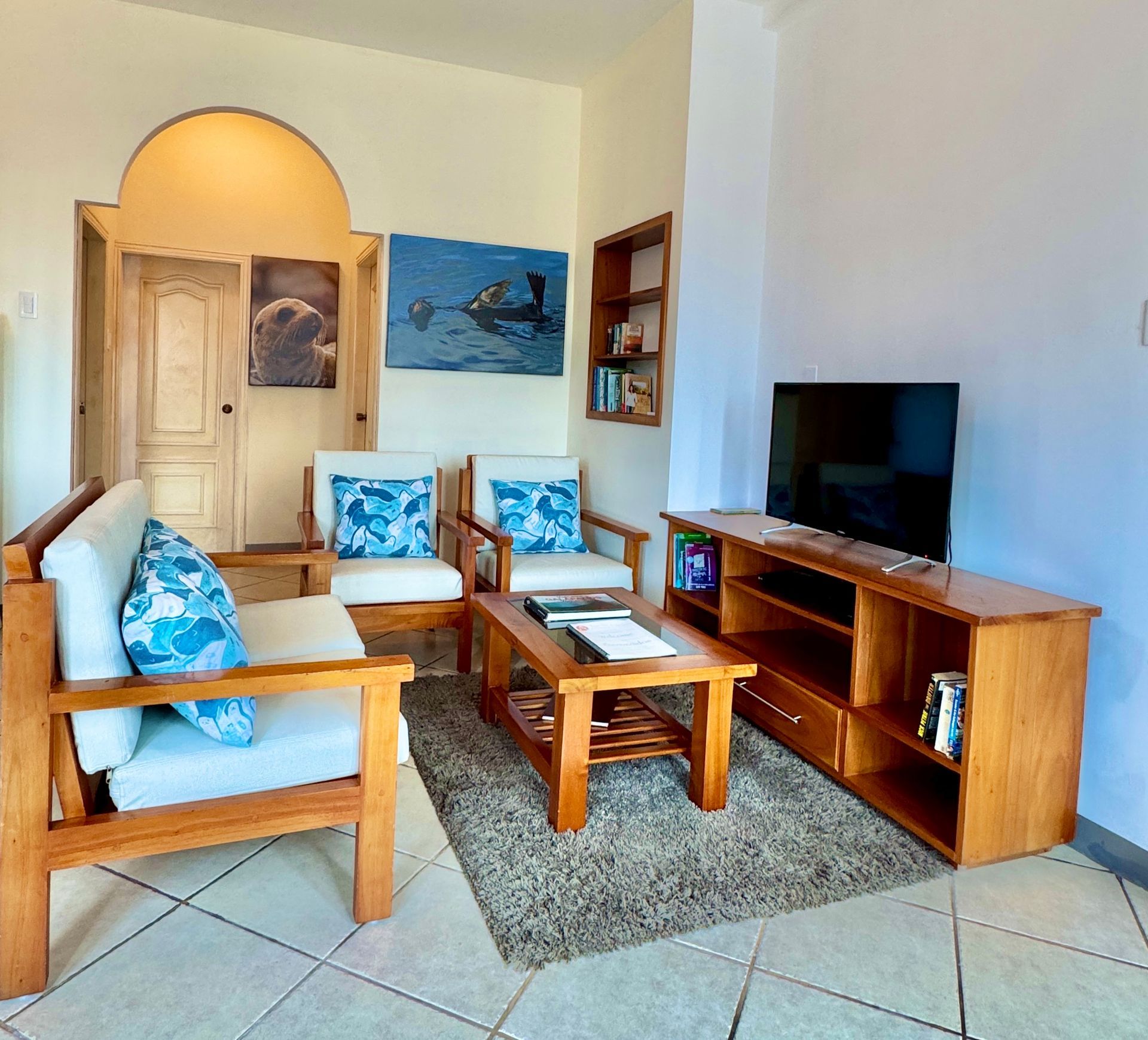 Living room with wooden furniture, including a sofa, armchairs, and a TV console. Blue and white cushions add pops of color.