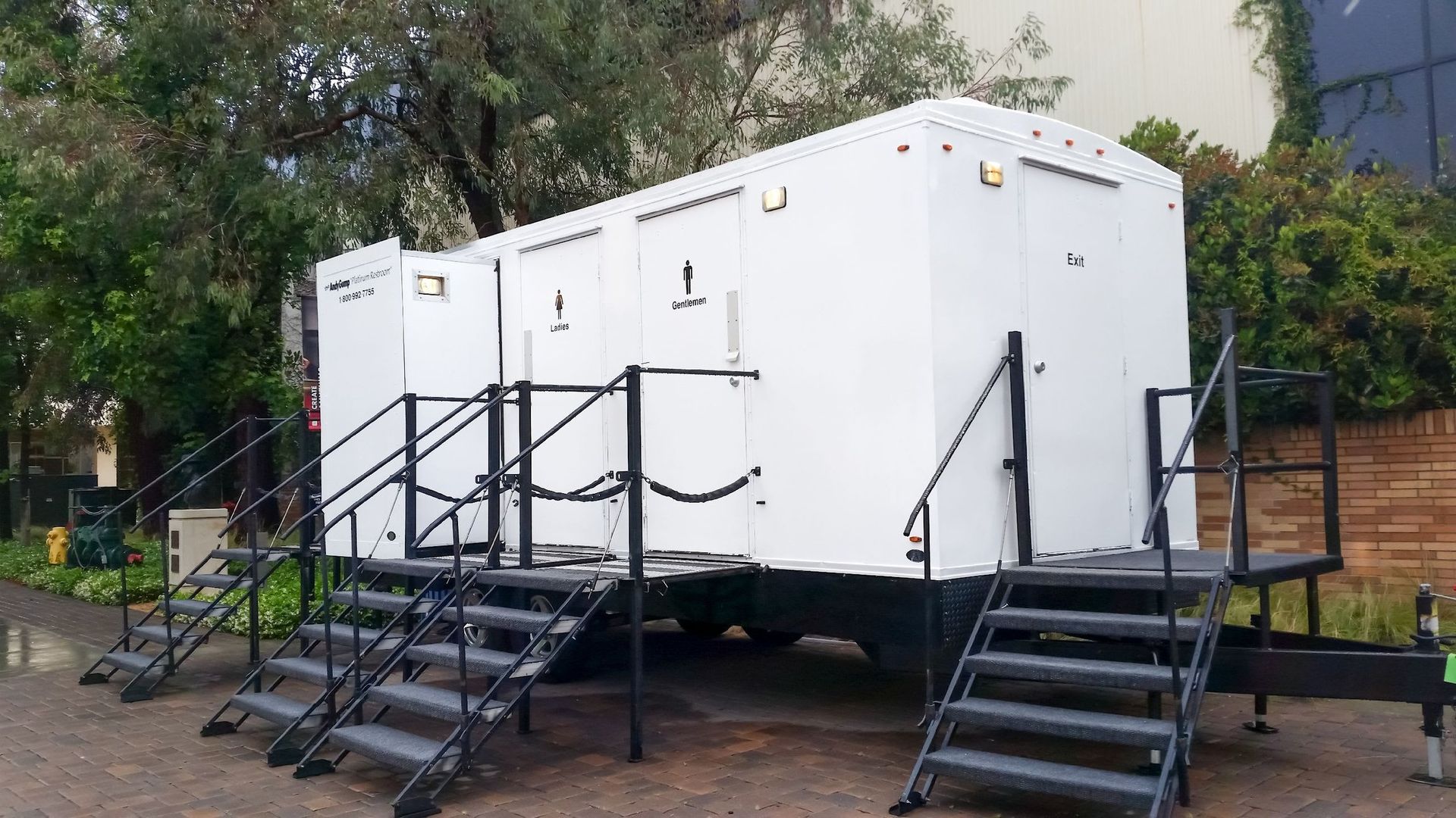 White portable restroom trailer with black stairs in an outdoor setting.