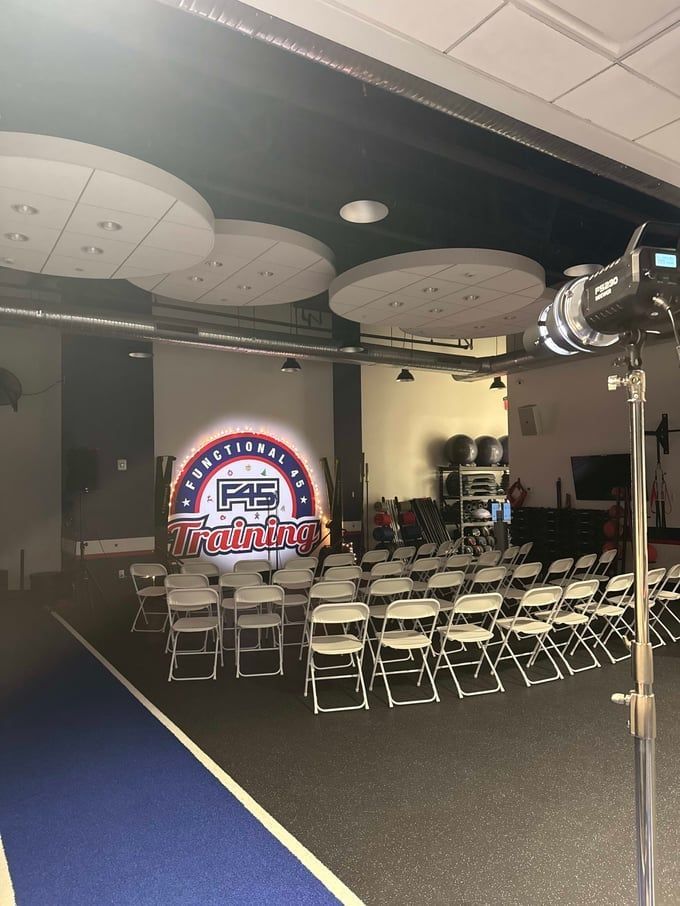 A fitness studio with rows of white chairs, a glowing logo on the back wall, and lighting equipment.