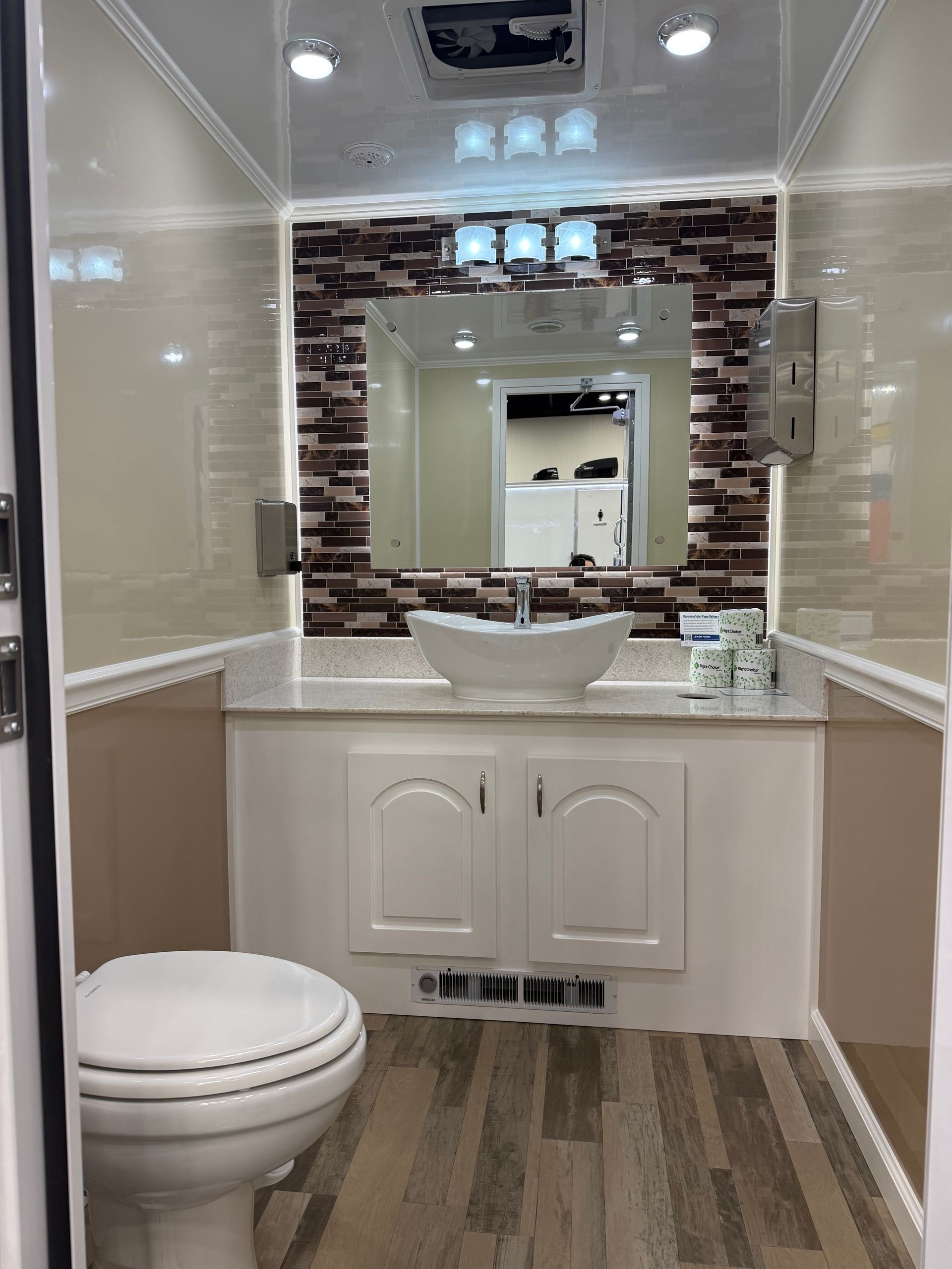A modern restroom interior with a toilet, vessel sink on a white vanity, a tiled backsplash, and wood-look flooring.