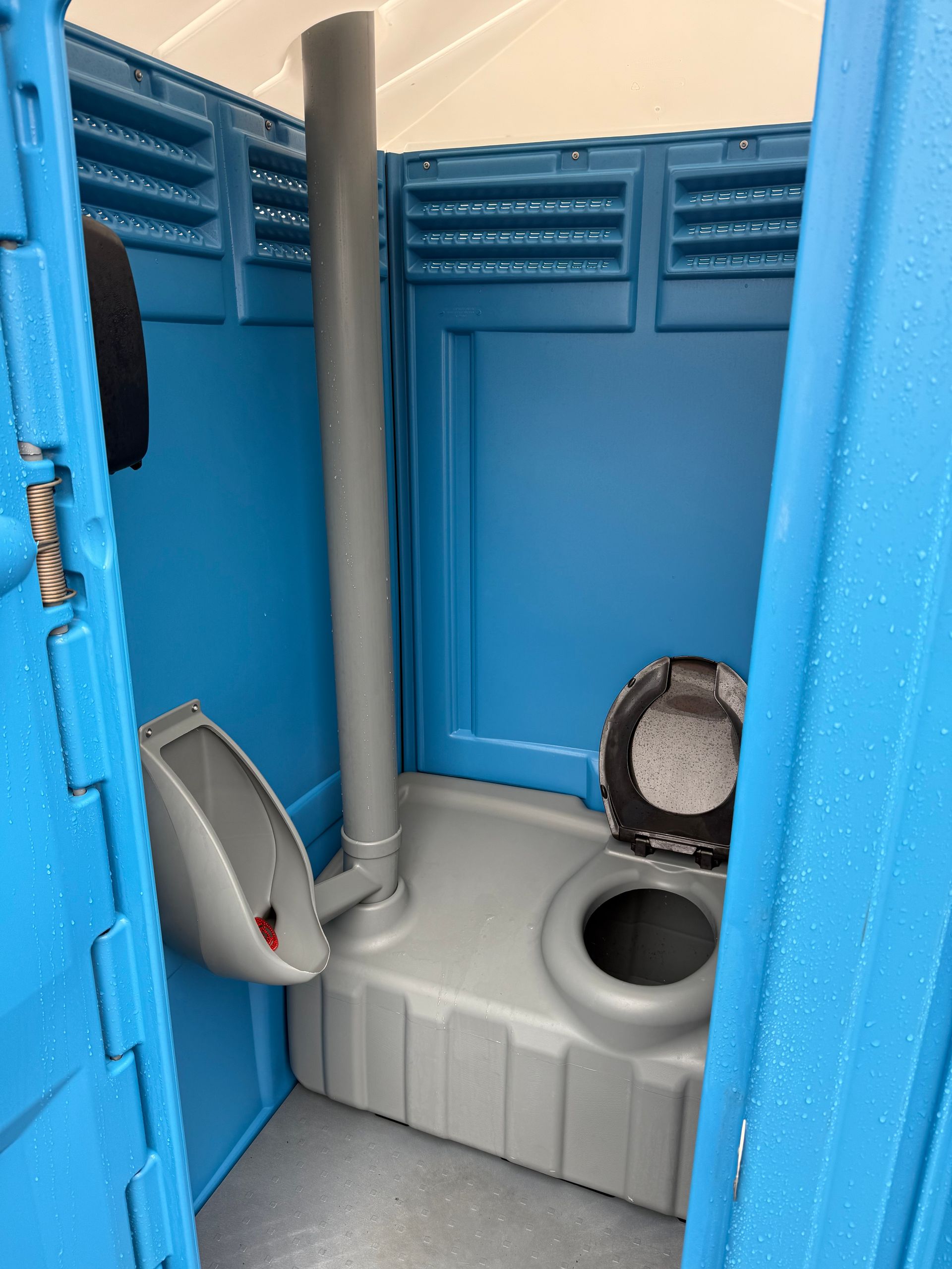 Interior view of a blue portable toilet featuring a gray tank with a toilet seat and a wall-mounted urinal.