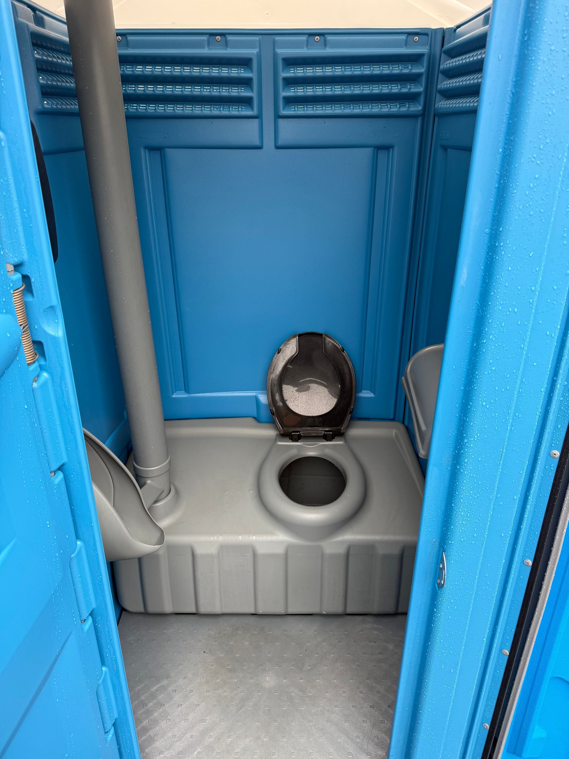 An interior view of a blue portable toilet featuring a grey plastic toilet seat, a side urinal, and a vent pipe.