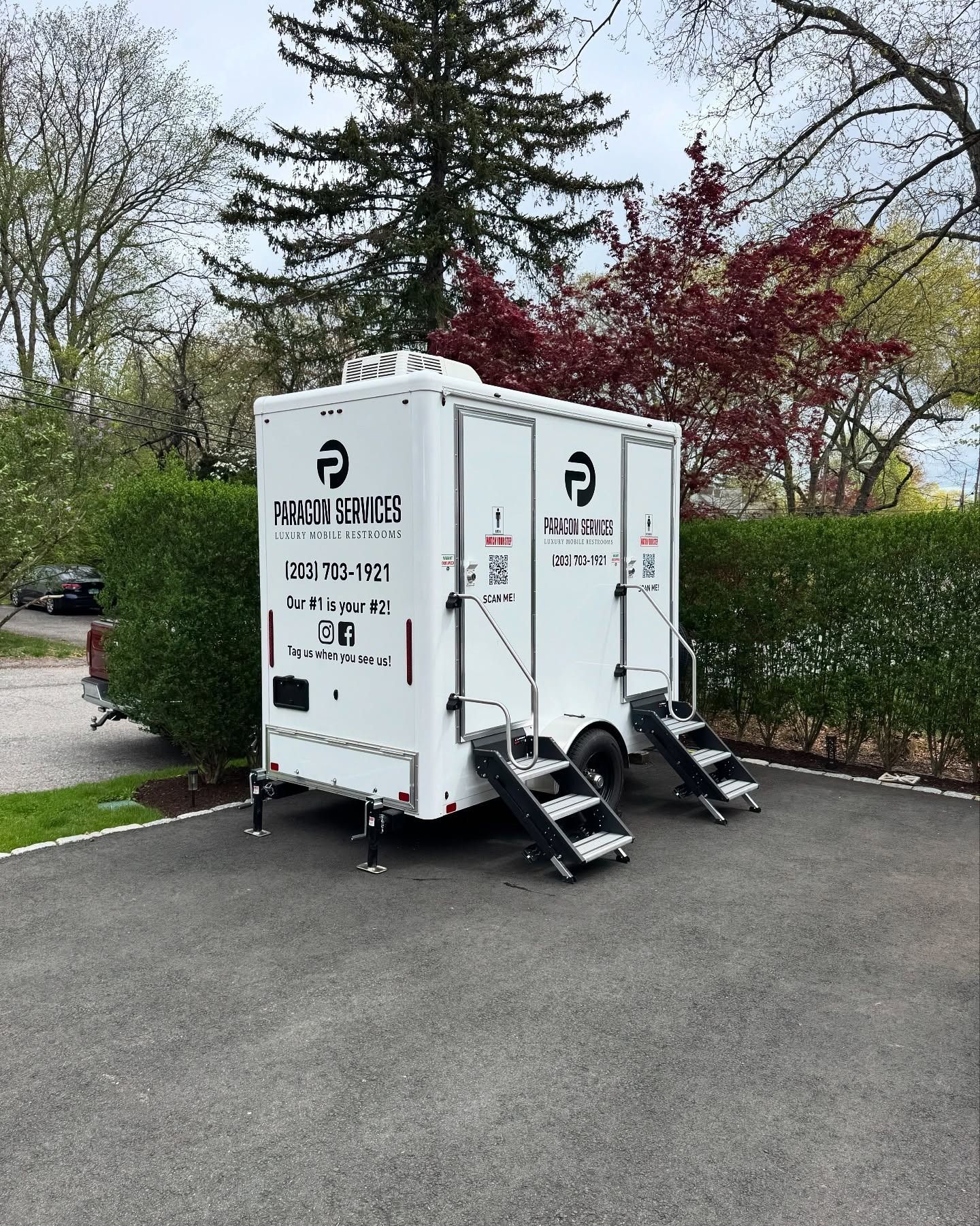 White portable restroom trailer on a paved driveway, with steps leading to two separate entrances.