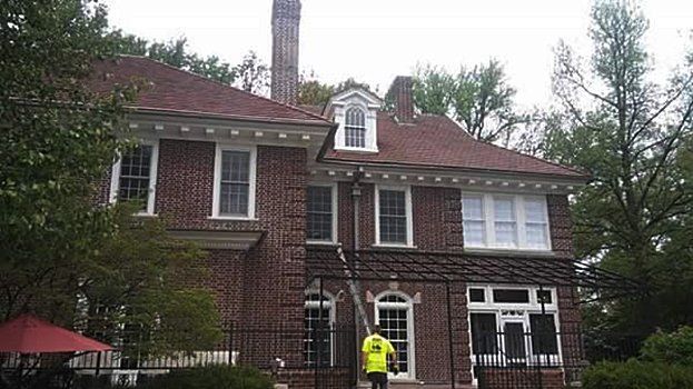 A man in a yellow vest is standing in front of a large brick house.
