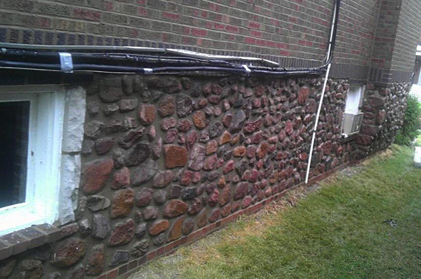 The side of a brick building with a stone wall and a window.