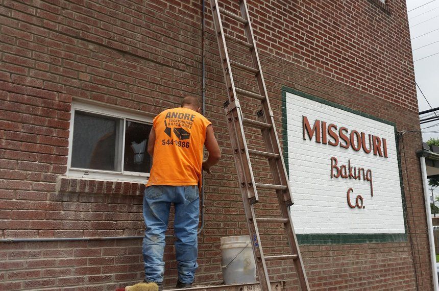 A man is standing on a ladder on the side of a brick building.
