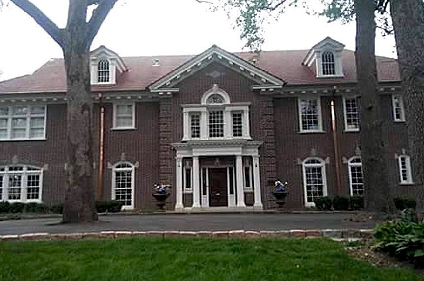 A large brick building with a red roof is surrounded by trees and grass.