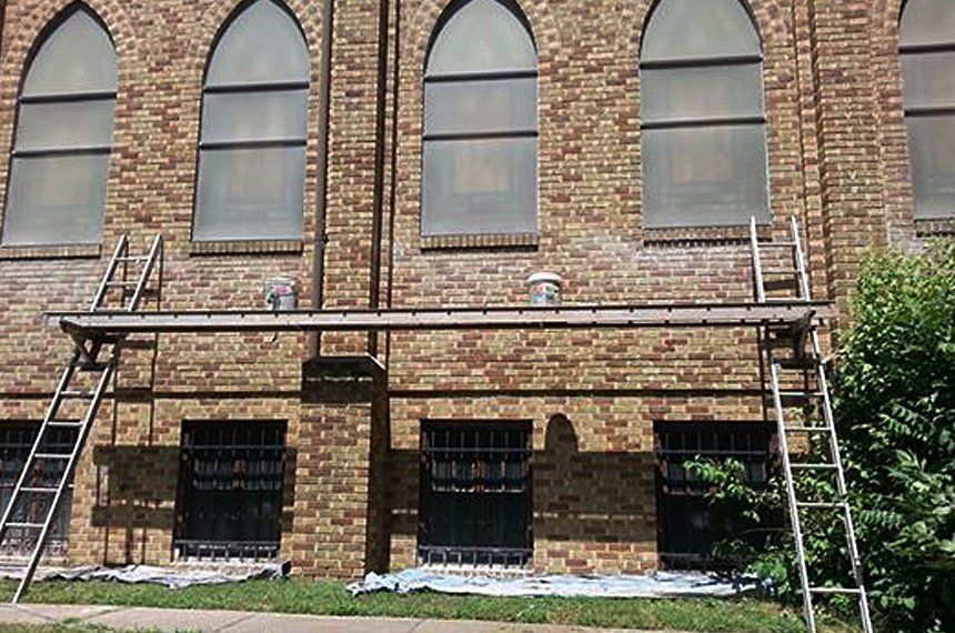 A brick building with arched windows is being painted