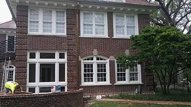 A large brick house with white windows is being painted.