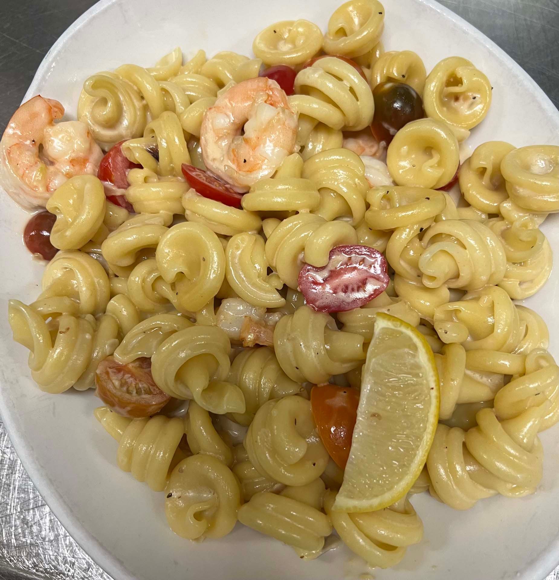 A white plate topped with pasta shrimp and tomatoes