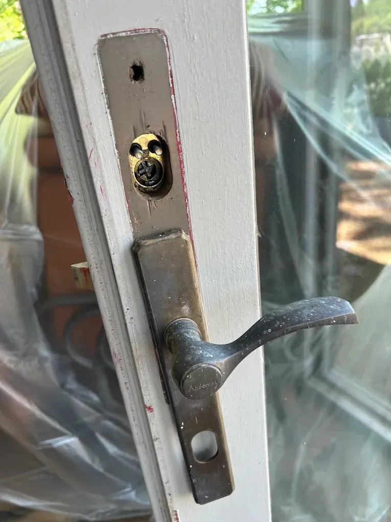 Door handle and lock plate on a white door, with peeling paint.