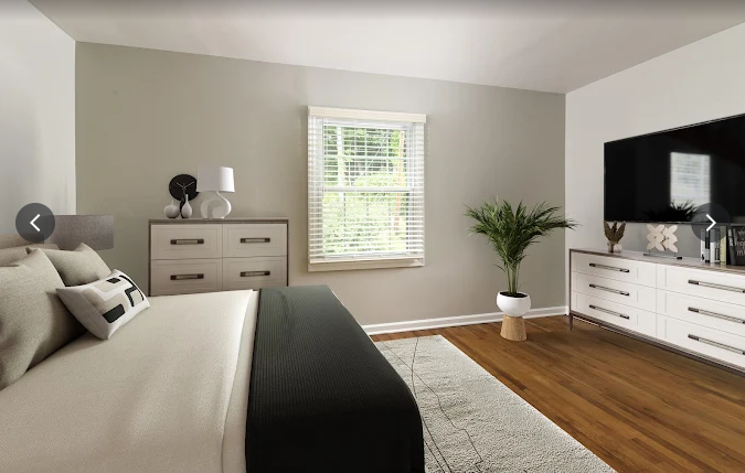 Bedroom with a bed, dressers, window, TV, and a plant. Neutral walls and oak wood floors.