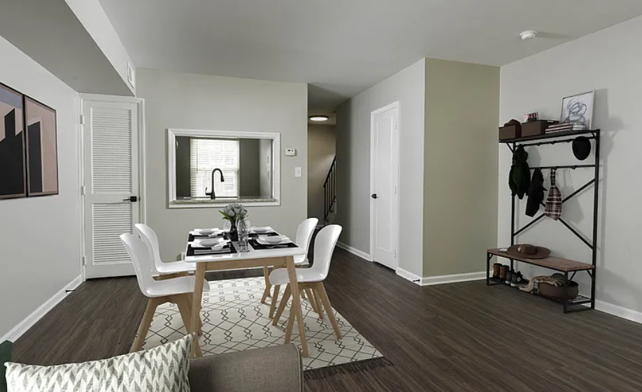 Dining area with table, chairs, and rug. Entrance hall has coat rack. Light walls, dark floors.