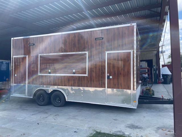 A brown wood-paneled trailer with two doors and a window, parked in an outdoor structure.