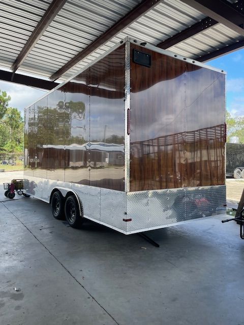 A shiny cargo trailer with brown panels and a silver base parked under a covered area.