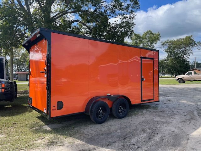 Orange cargo trailer with black trim and tires parked on gravel.