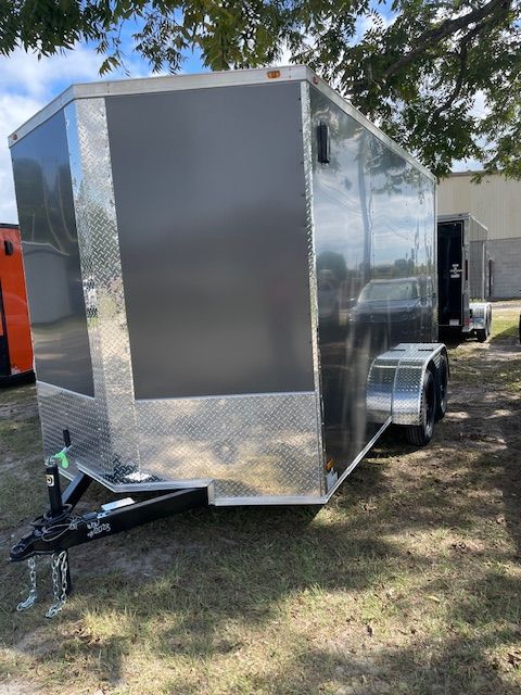 Silver and black enclosed cargo trailer parked on grass, with a black hitch.
