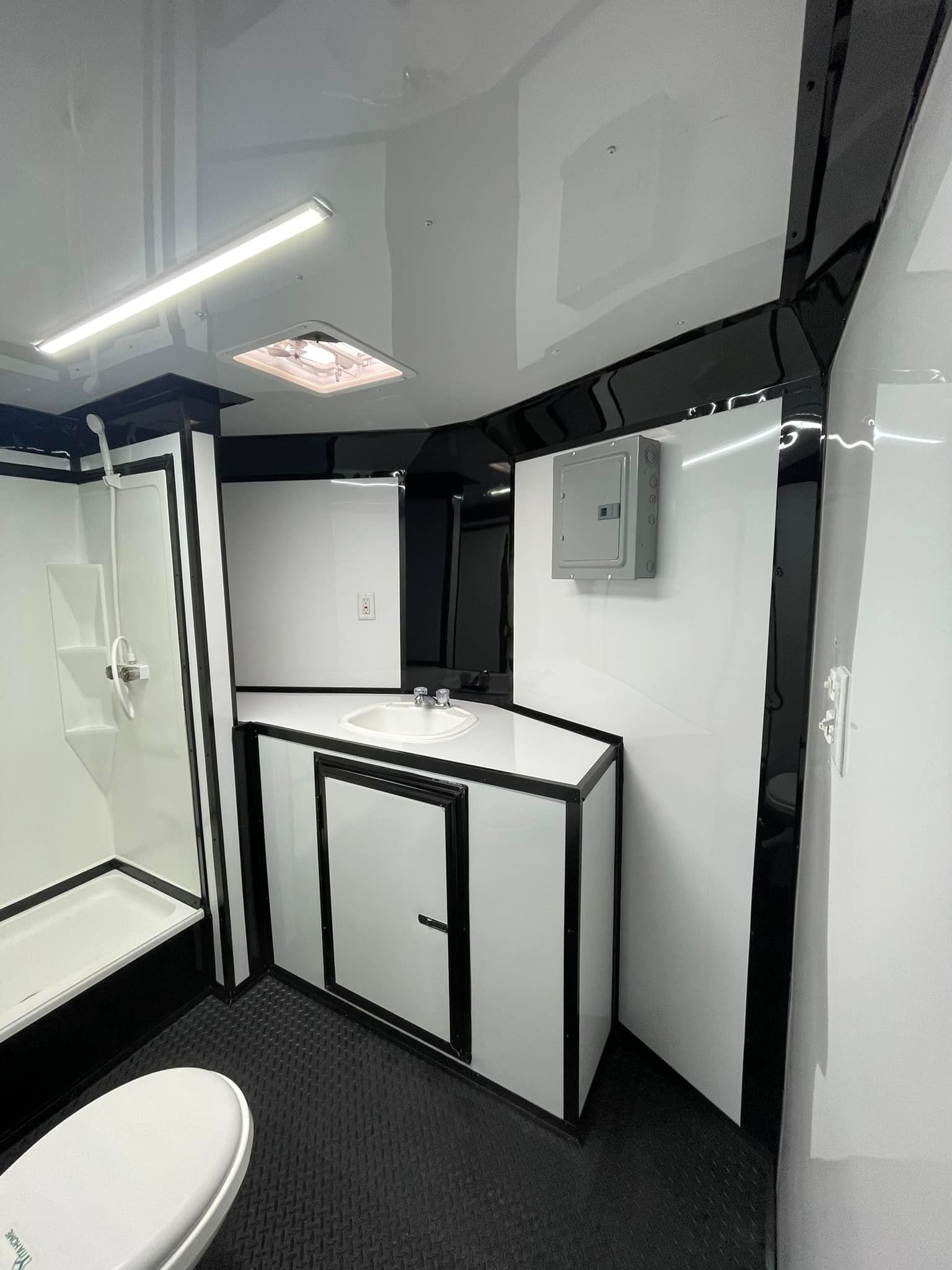 Interior of a trailer bathroom with white walls, black trim, and a shower, sink, and toilet.